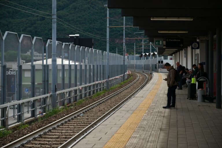People wait on a train station platform next to tracks.